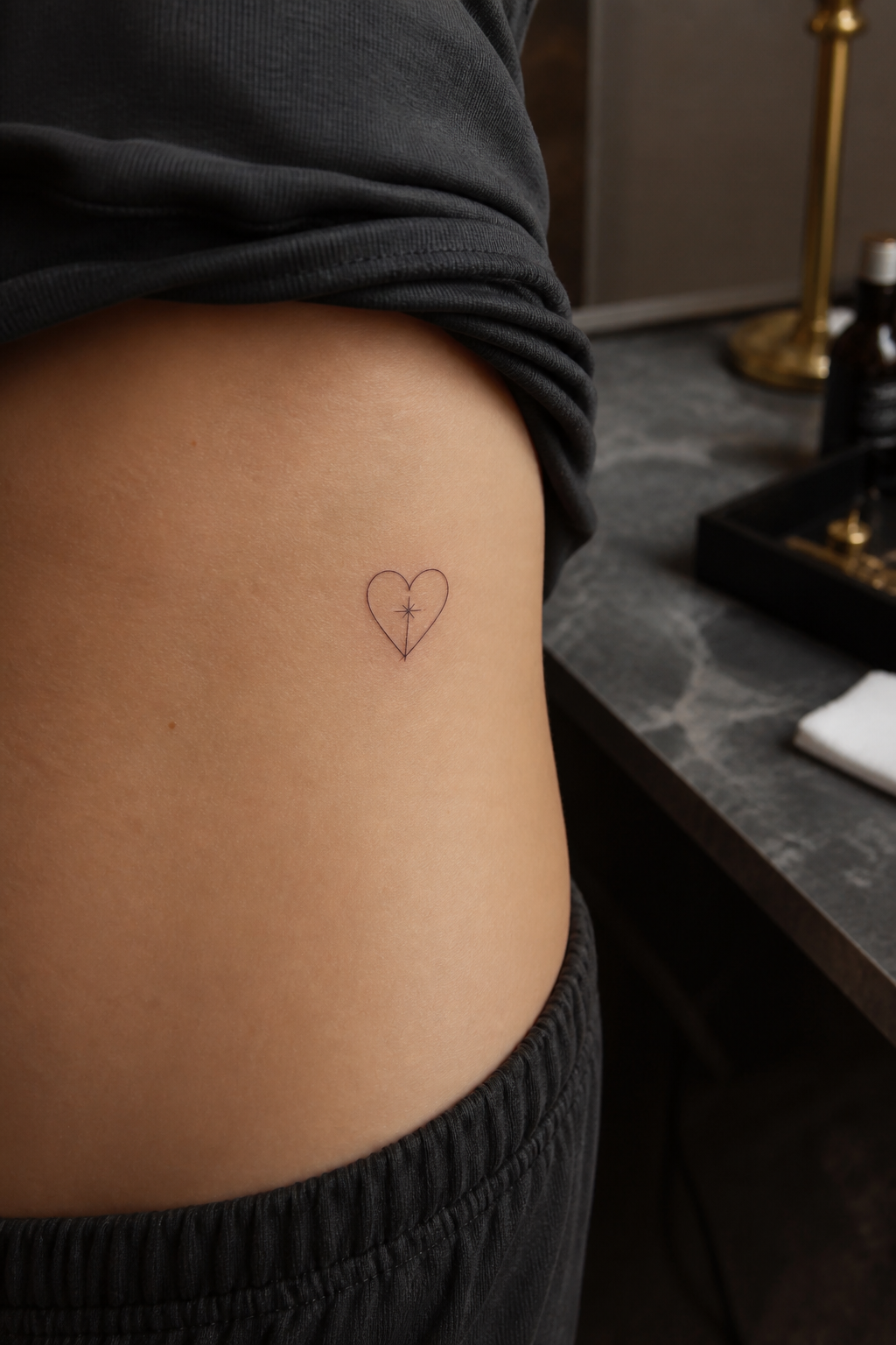 Tiny heart outline tattoo with a subtle cross on the side torso